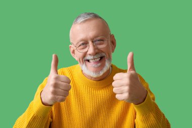Gözlüklü mutlu yaşlı adam yeşil arka planda baş parmak gösteriyor, yakın plan. Ulusal Büyükbaba Günü
