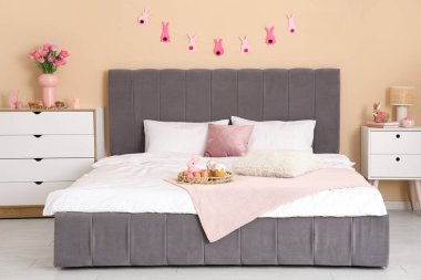 Konforlu yatağı, çelengi ve şifoniyerinde lale çiçekleri olan şenlikli bir yatak odası. Paskalya kutlaması