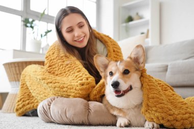 Genç kadın ve Corgi köpeği evde yerde turuncu ekoseli.