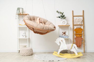 Çocuk odasının içinde sallanan koltuk, merdiven ve bebek kıyafetleri var.