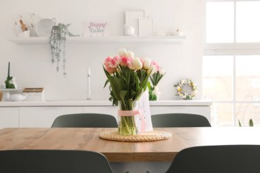 Mutfaktaki yemek masasında lale ve paskalya kartı olan vazo.