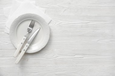 Çatal bıçaklı tabak ve beyaz ahşap arka planda kağıt peçete.
