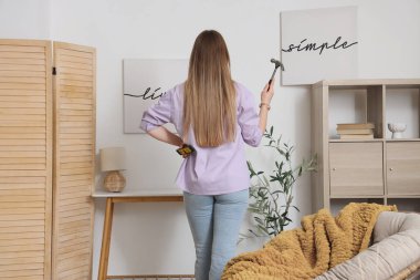 Çekiçli ve katlı genç bir kadın evdeki ışıklı duvarlara, arka manzaraya posterler asıyor.