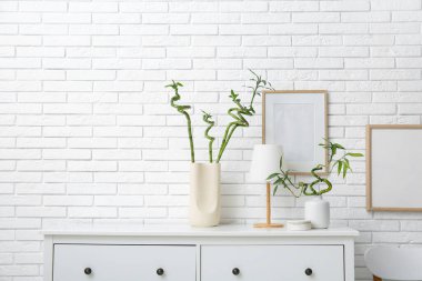 Bambu saplı vazolar ve beyaz tuğla duvarın yanındaki çekmecelerde lamba.