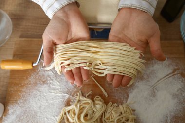 Makarna tutan genç bir kadın mutfak masasının yanında makineyle yapılmış.