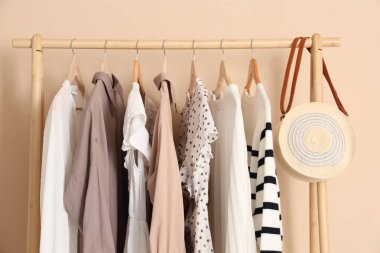 Ahşap raf, şık kıyafetler ve bej duvarın yanında el çantası.