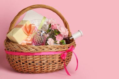 Bahar çiçekleriyle hediye sepeti ve pembe arka planda parfüm.