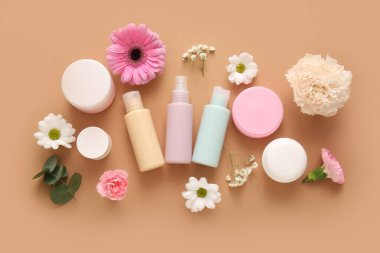 Farklı kozmetik ürünleri ve kahverengi arka planda güzel çiçekler.