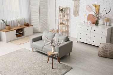 Oturma odasının içinde kanepe ve çiçek açan dallar var.