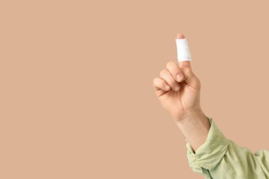 Bej arka planda bandajlı parmağı olan bir erkek el.