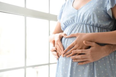 Hamile çift evdeki pencerenin yanında kalp hareketi yapıyor, yakın çekim.