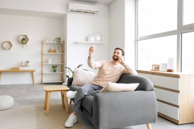 Evdeki klimanın yanındaki kanepede cep telefonuyla konuşan genç adam.