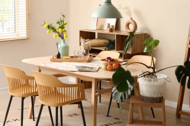 Odanın içinde yemek masası, ahşap raf ünitesi ve palmiye bitkisi var.