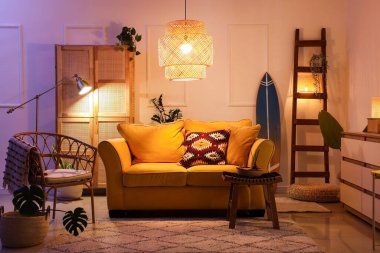 Şık oturma odasının içinde sarı kanepe, parlak lambalar ve akşamları sörf tahtası.