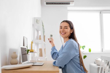 Masadaki genç kadın oturma odasındaki klimayı açıyor.