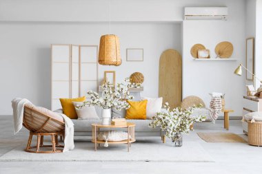 Kanepe, koltuk ve vazolarda çiçek açan dallarla aydınlık oturma odasının içinde.