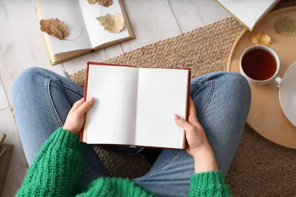 Boş kitabı ve sonbahar yaprakları olan bir kadın evde, halıda oturuyor.