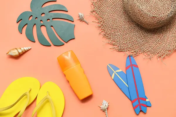 Parmak arası terlikli mini sörf tahtaları, güneş kremi ve turuncu arka planda hasır şapka. Yaz konsepti