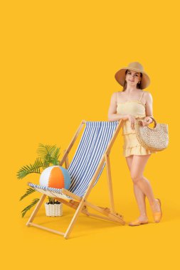 Sarı arka planda kumsal çantalı ve şezlonglu güzel kadın.