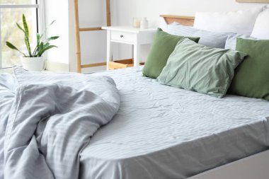 Yatak odasında yumuşak yeşil yastıkları ve buruşuk gri battaniyesi olan rahat bir yatak.