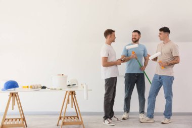 Odadaki ışık duvarının yanında boya silindirli ve fırçalı genç adamlar