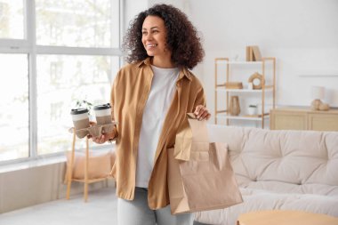 Evinde kahve fincanı ve kağıt torbaları olan genç bir Afro-Amerikalı kadın. Yemek dağıtım servisi.