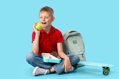 Beslenme çantalı küçük çocuk mavi arka planda elma yiyor.