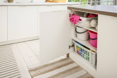 Modern mutfakta temizlik malzemeleri, depolama sepetleri ve kovalarla dolu bir dolap.