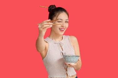 Kırmızı arka planda lezzetli ramen yiyen genç Asyalı kadın.