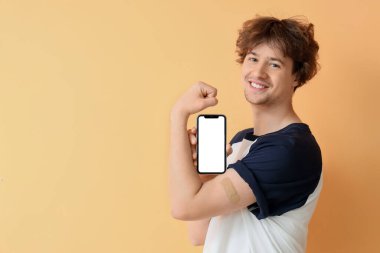 Uygulamalı tıbbi yaması ve bej arka planda boş cep telefonu olan genç bir adam. Aşılama kavramı