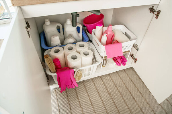 Baskets with different cleaning supplies and paper towels under sink in kitchen