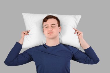 Gri arka planda uyuyan şık pijamalı yakışıklı bir genç.
