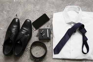 Gri grunge arka planında gömlek, cep telefonu ve ayakkabıları olan erkek aksesuarları. Üst görünüm