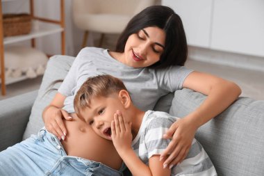 Oturma odasında ağzı açık bir şekilde annesinin karnına yaslanan şaşkın çocuk.