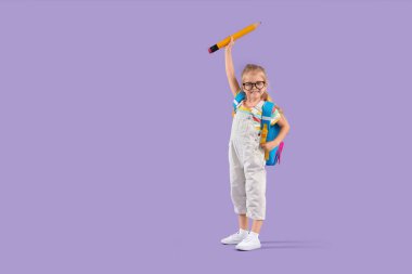 Leylak arka planında büyük bir kalemi ve sırt çantası olan sevimli küçük bir kız öğrenci.