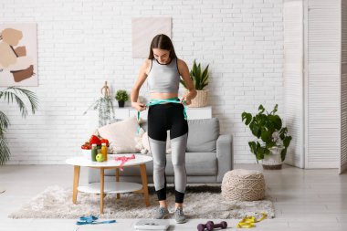 Evde belini ölçen genç bir kadın. Diyet kavramı