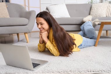 Evdeki halının üzerinde dizüstü bilgisayarla görüntülü sohbet eden güzel bir kadın.