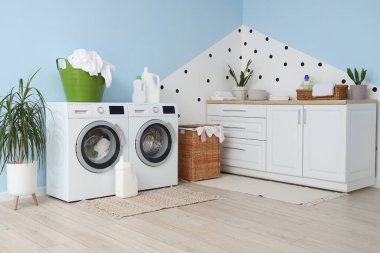 Çamaşır makineleri, deterjanlar ve sepetlerle çamaşır odasının içinde.