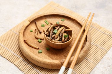 Tahta kase, kızarmış kurtçuklar ve yeşil soğanlı beyaz arka plan.