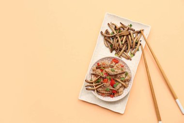 Bir kase kızarmış kurtlu pilav ve turuncu arka planda yeşil soğan.