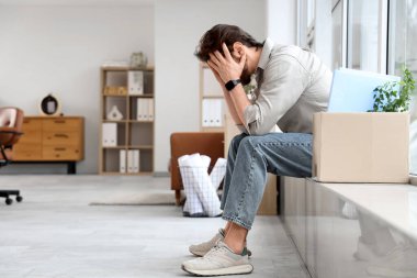 Ofisteki pencere eşiğinde oturan üzgün genç adam.