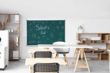 Sınıfın içinde karatahta, raf üniteleri ve masalar var. Okul yılı sonu.