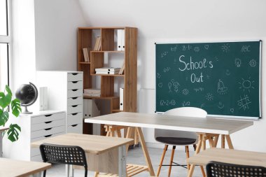 Sınıfın içinde karatahta, raf ünitesi ve masalar var. Okul yılı sonu.