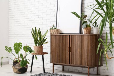 Fotoğraf çerçeveli giyinen ve oturma odasındaki beyaz tuğla duvarın yanında farklı ev bitkileri olan.