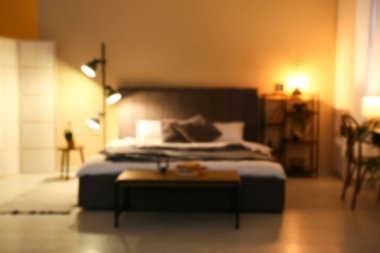Yatak odasının şık bir iç mekanı. Rahat gri yatak ve gece parlayan lamba, bulanık görüş.
