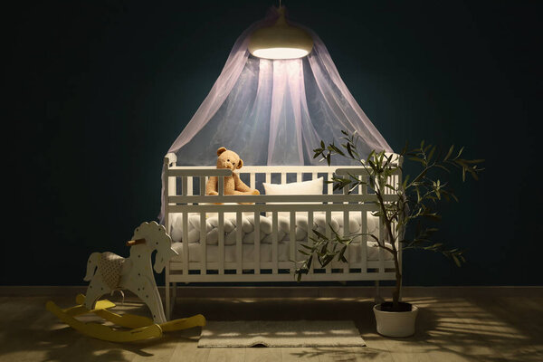 Детская спальня с детской кроваткой, комнатным стеклом и светящимся светильником ночью