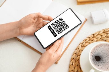 Female hands with mobile phone and notebook on light background, closeup