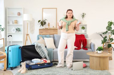 Cep telefonu ve kahve fincanı olan genç bir kadın eve gitmek için bavulunu hazırlıyor.