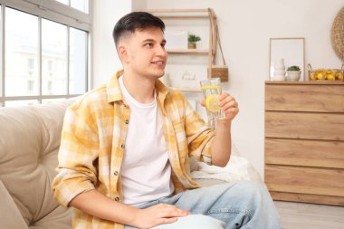 Evdeki kanepede oturan limonlu su dolu genç adam.