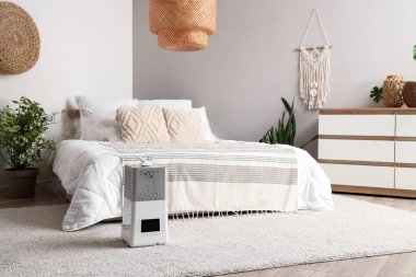 Yatak odasının içinde klozet, ev bitkileri ve yatağın yanında modern nemlendirici var.